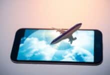 Um smartphone exibindo vários aplicativos de viagem com um avião decolando ao fundo, simbolizando a compra de passagens aéreas pelo celular