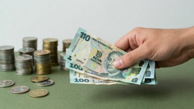 Pessoa trocando dinheiro em um balcão de câmbio com símbolos de diferentes moedas ao fundo