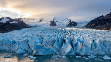 Paisagem de uma imponente geleira islandesa ao nascer do sol, com detalhes de gelo azul e montanhas ao fundo