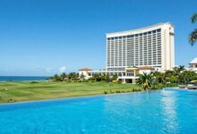 Vista panorâmica de uma paisagem de luxo com hotel cinco estrelas, campo verdejante, piscina infinita e céu azul cristalino