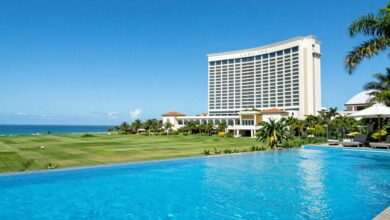 Vista panorâmica de uma paisagem de luxo com hotel cinco estrelas, campo verdejante, piscina infinita e céu azul cristalino
