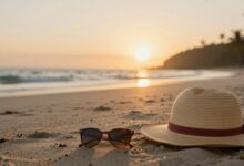 Praia deserta com mala e chapéu ao pôr do sol, simbolizando aventura e relaxamento de uma viagem de última hora