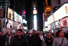 Vista panorâmica da Times Square à noite, com luzes de néon e multidões de pessoas aproveitando a energia vibrante da cidade.