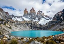 Uma vista panorâmica das montanhas imponentes de Torres del Paine na Patagônia, com um lago azul-turquesa em primeiro plano sob um céu dramático.