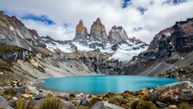 Uma vista panorâmica das montanhas imponentes de Torres del Paine na Patagônia, com um lago azul-turquesa em primeiro plano sob um céu dramático.