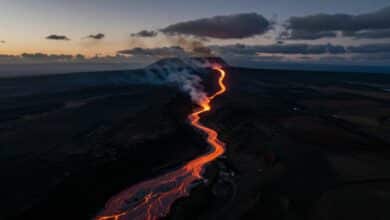 Vista aérea de um rio de lava laranja brilhante escorrendo pela paisagem vulcânica escura do vulcão Kīlauea no Havaí ao entardecer.