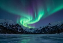Uma espetacular aurora boreal com tons de verde e roxo dançando no céu estrelado sobre uma paisagem de montanhas nevadas e um lago congelado.