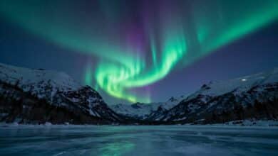 Uma espetacular aurora boreal com tons de verde e roxo dançando no céu estrelado sobre uma paisagem de montanhas nevadas e um lago congelado.