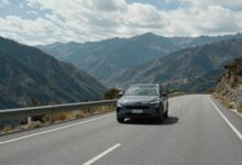 Uma estrada sinuosa com uma bela paisagem de montanhas ao fundo, com um carro moderno viajando por ela, simbolizando a liberdade de uma viagem de carro.