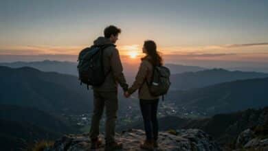 Casal aventureiro de mãos dadas no topo de uma montanha ao nascer do sol, com um vale enevoado abaixo deles, transmitindo uma sensação de conquista e romance.