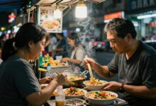 Uma movimentada rua de Bangkok à noite, iluminada por letreiros de neon, com uma barraca de comida de rua em primeiro plano preparando Pad Thai em uma wok flamejante.