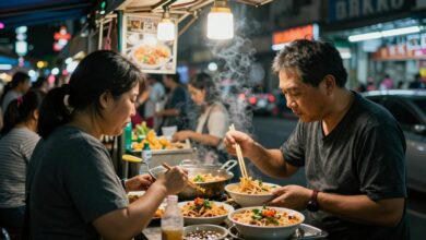 Uma movimentada rua de Bangkok à noite, iluminada por letreiros de neon, com uma barraca de comida de rua em primeiro plano preparando Pad Thai em uma wok flamejante.